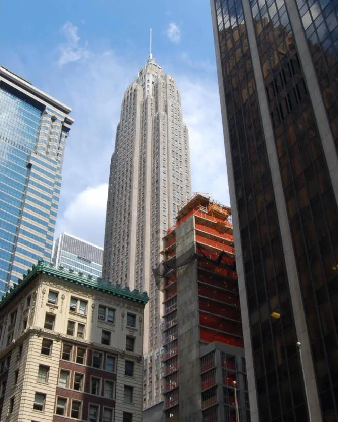 A tall setback Art Deco limestone tower with a slender spire, seen between older and newer buildings