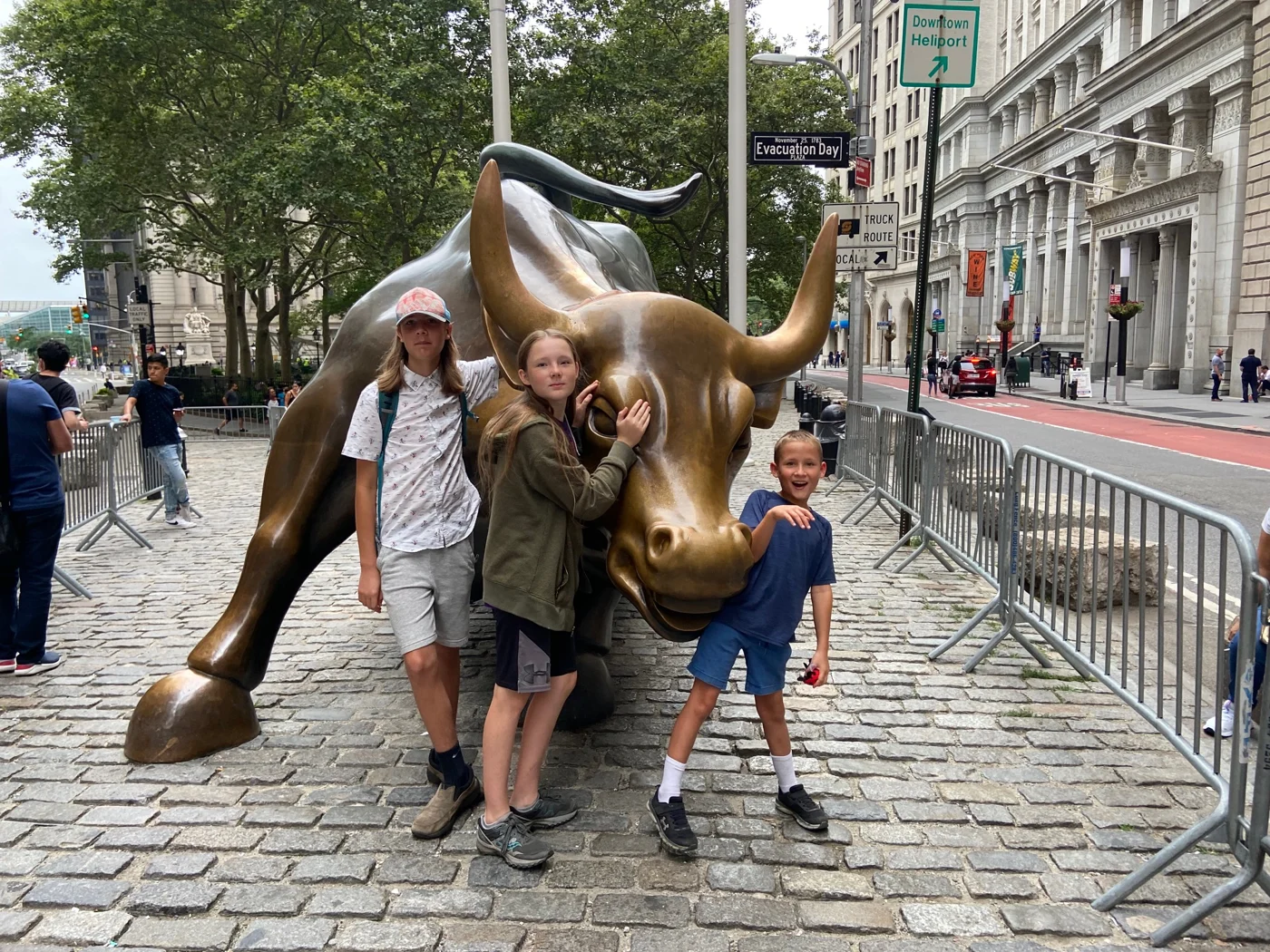 Three children posing with the bronze Charging Bull sculpture on a cobblestone plaza at Bowling Green