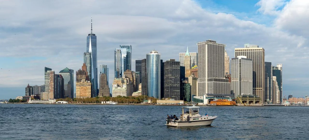 The Lower Manhattan skyline across the water from Governors Island, with a small fishing boat in the foreground