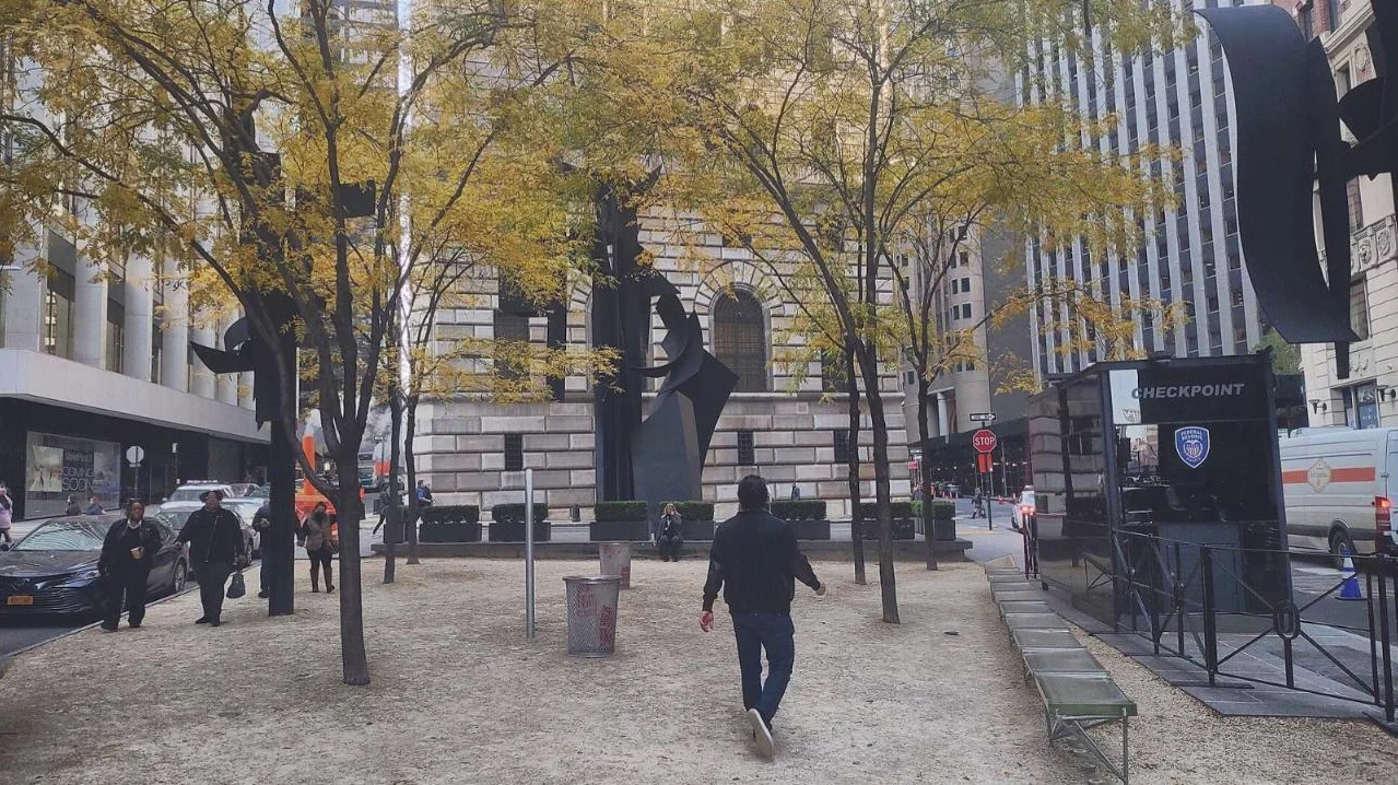 Tall black abstract sculptures among yellow autumn trees in a small triangular plaza