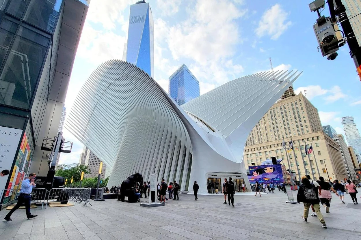 The white ribbed wings of the Oculus transit hub spreading over a plaza, with One World Trade Center rising behind