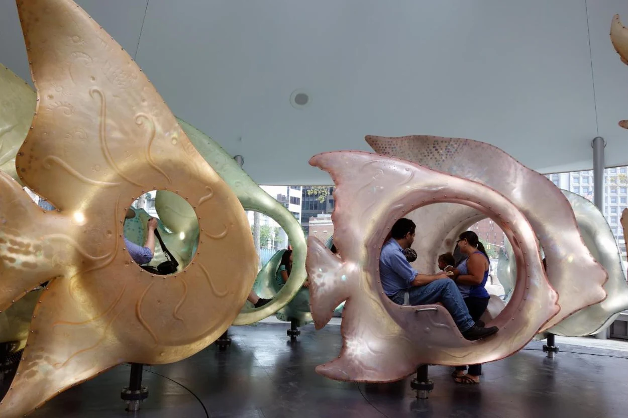 People seated inside large pearly pink and gold fish-shaped seats under a white ceiling