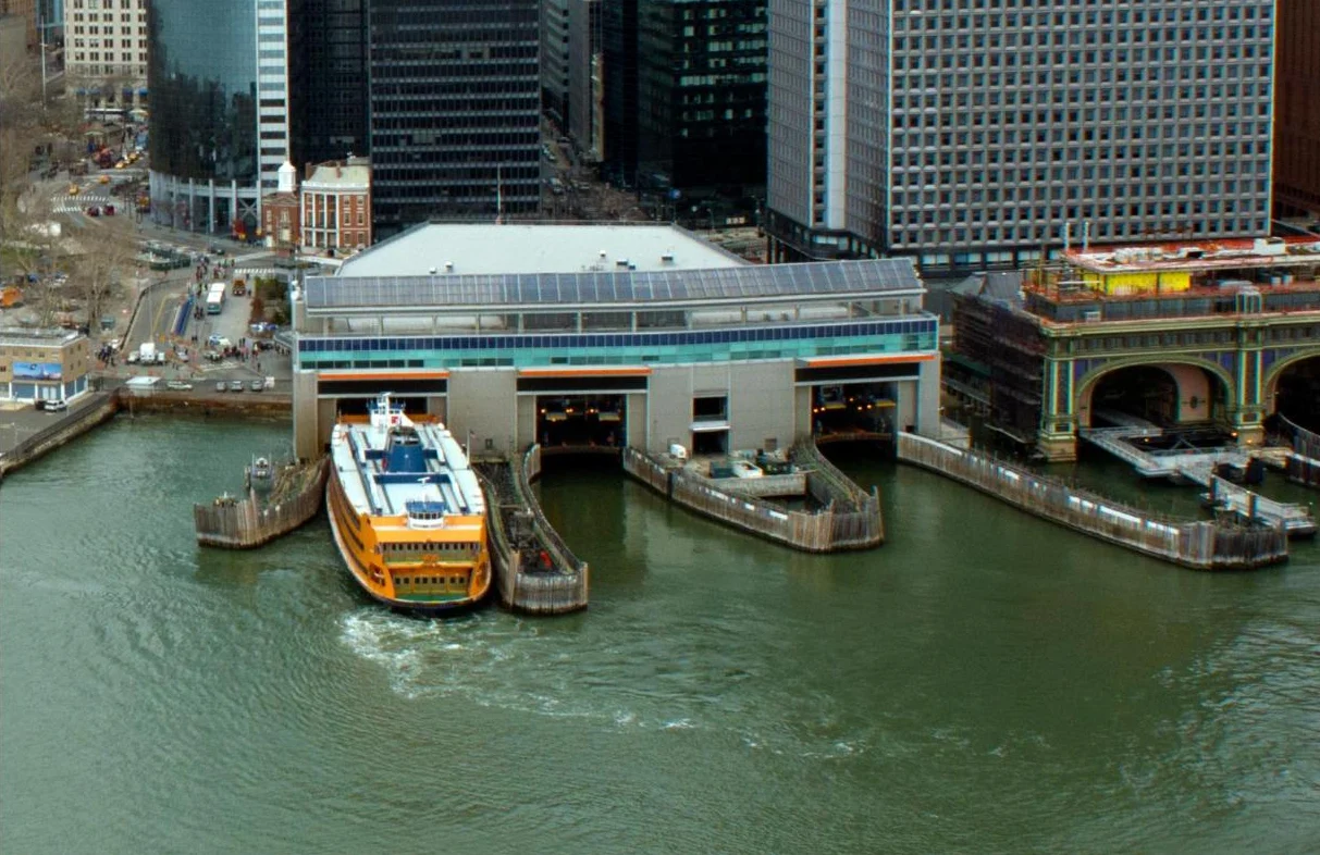 An orange ferry docked at a terminal on the water at the tip of Manhattan