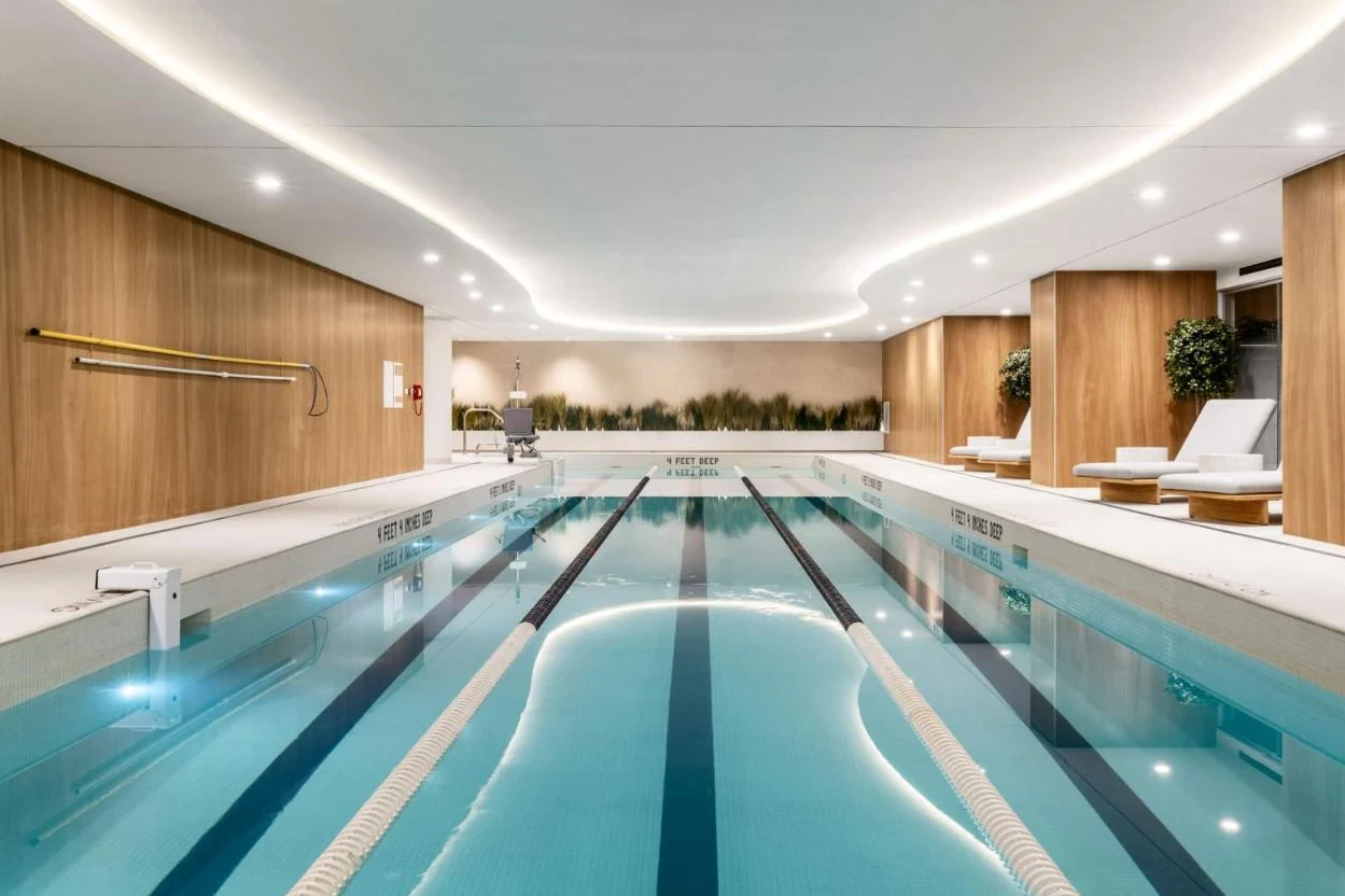 An indoor lap pool with wood-paneled walls, lane lines and white lounge chairs