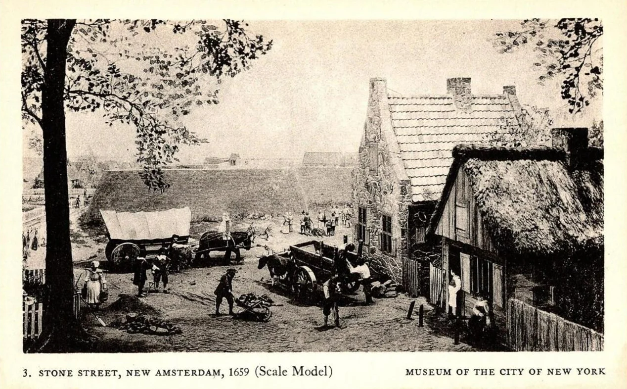 A black and white postcard of a scale model showing a dirt street with a covered wagon, oxen and gabled Dutch houses