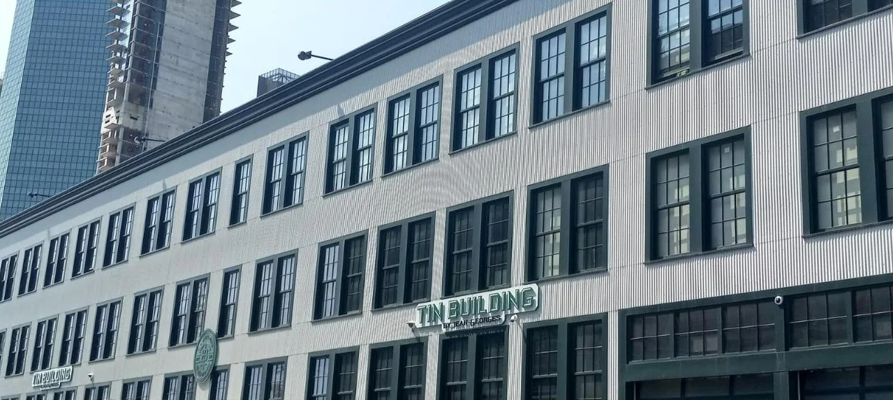 A long three-story building clad in corrugated metal with green-trimmed windows and a Tin Building sign