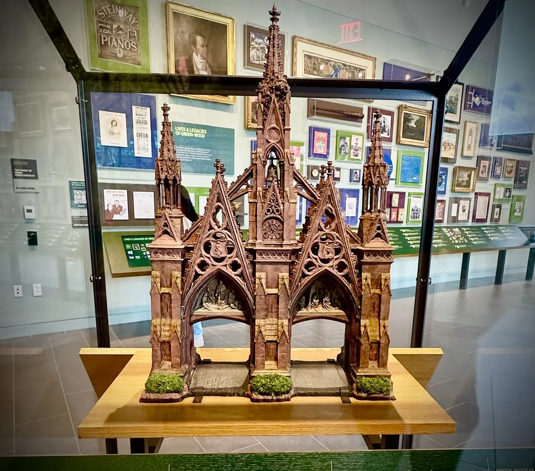 A detailed scale model of Green-Wood’s Gothic Revival main gate in a glass case, with exhibits on the walls behind it