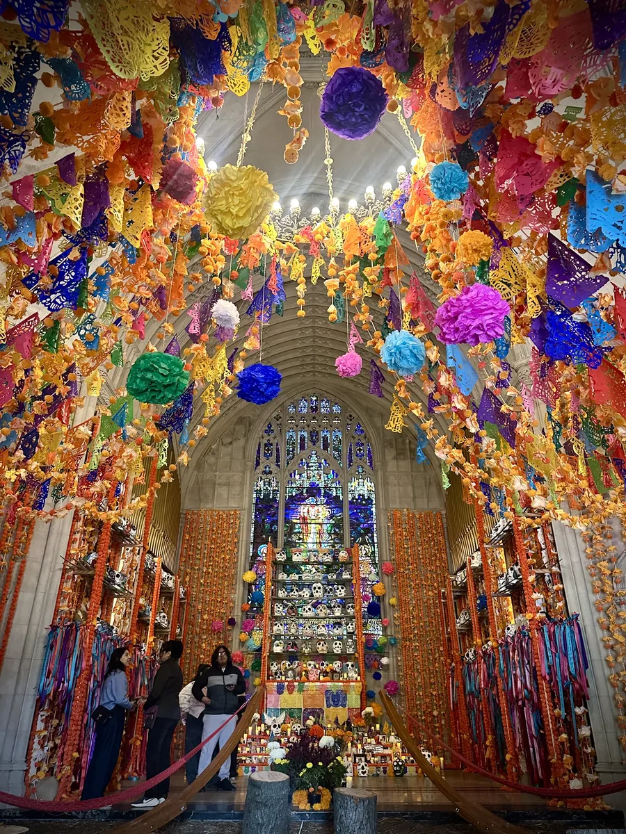The Chapel interior hung with papel picado, paper flowers and marigold garlands, with an altar of painted skulls beneath the stained-glass window