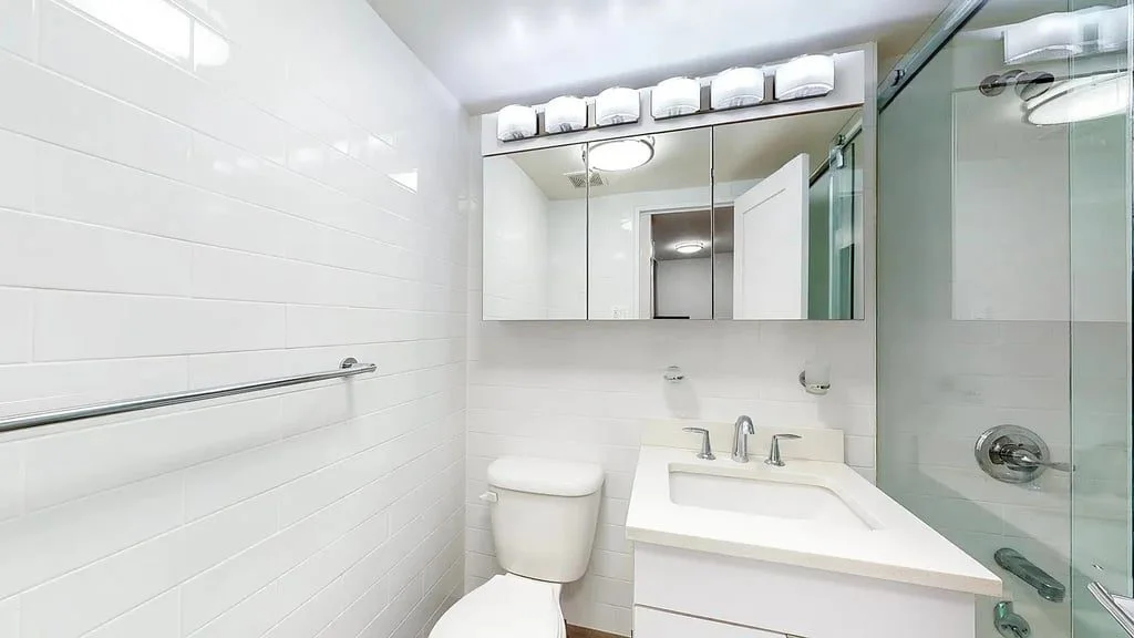 A white tiled bath with a glass shower and a mirrored medicine cabinet