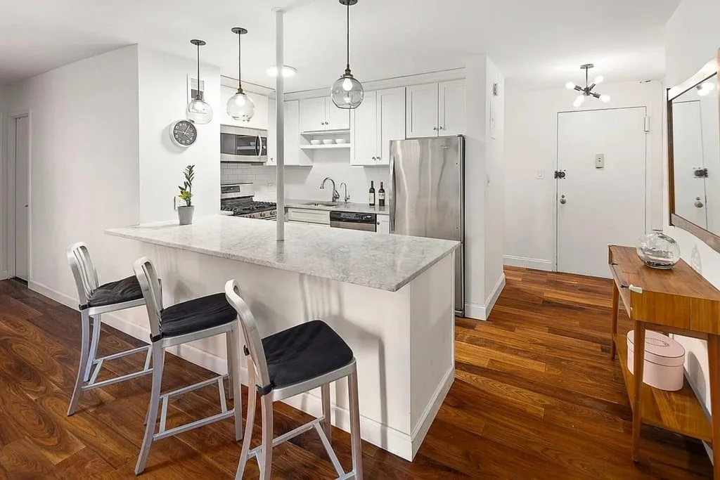 An open kitchen with a marble-topped island, bar stools, white cabinets and stainless steel appliances