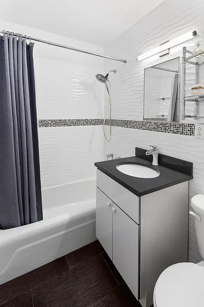 A bath with a black stone vanity top, white cabinet and tiled shower