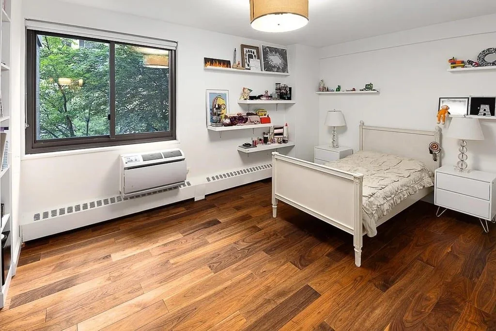 A bright bedroom with a white daybed, wall shelves and wide windows