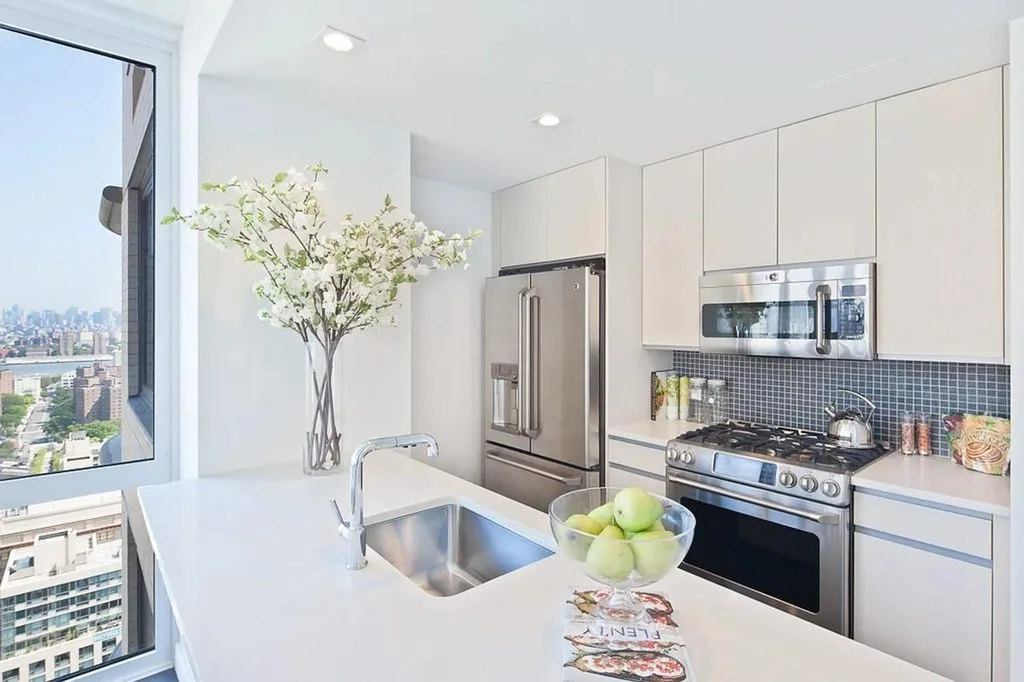 An open kitchen with white cabinets, a stainless range and a window over the city