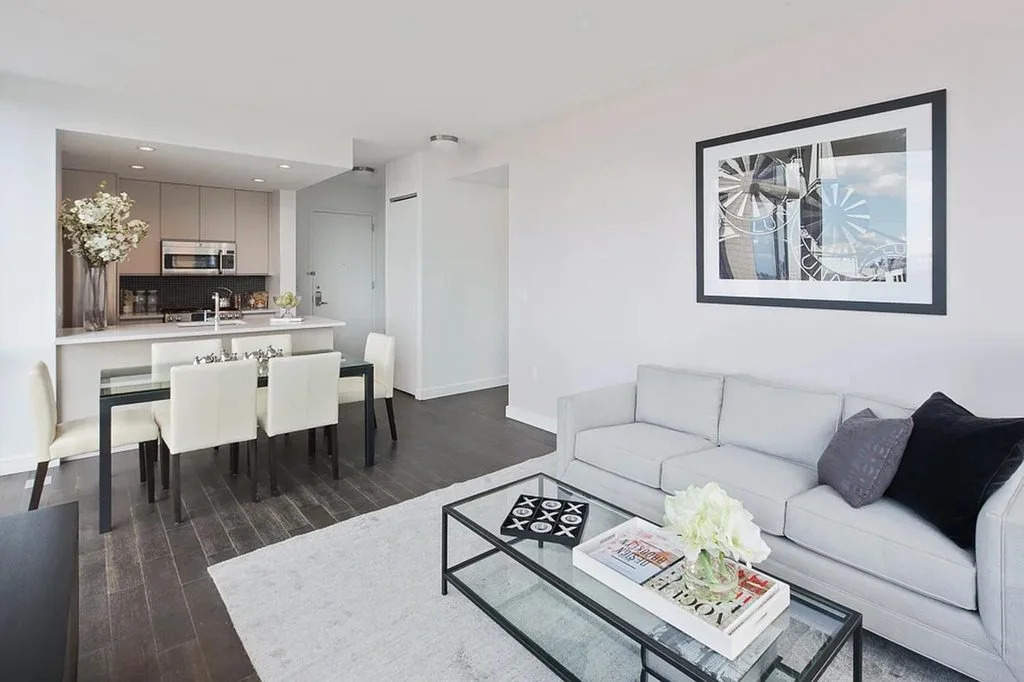A living room with a white sofa and a glass coffee table opening onto an open kitchen and dining table