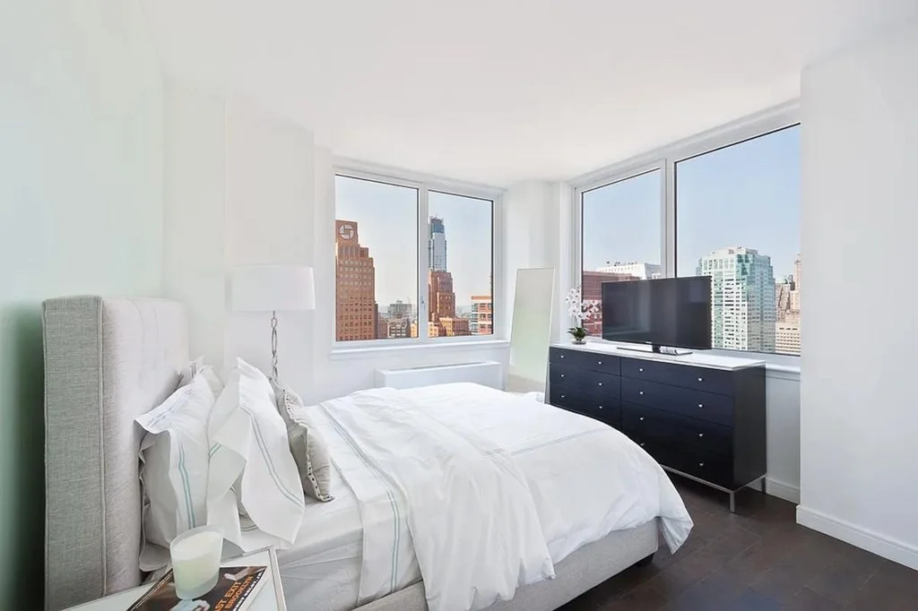 A bright bedroom with an upholstered headboard and a view of the skyline
