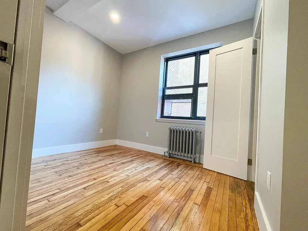 A bedroom with a window, a radiator and warm hardwood floors